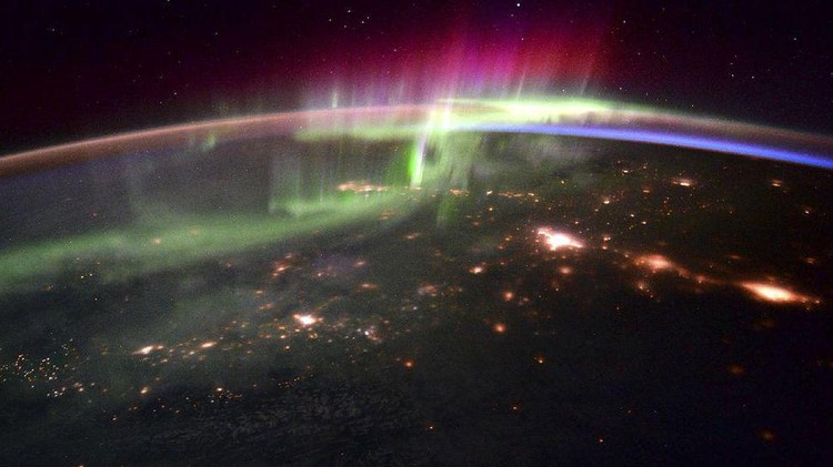 Penampakan spektakuler aurora seakan menyelimuti Bumi, dari titik 240 kilometer di atas sana memperlihatkan cahaya hijau aurora tinggi di atmosfer sementara di kejauhan, ada sinar kemerahan. Sedangkan di bawahnya adalah area awan-awan yang berarak di atas lautan.