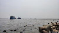 Terlihat kapal-kapal kayu ada di kejauhan. Di tepian daratan, ada beton-beton pemecah ombak.