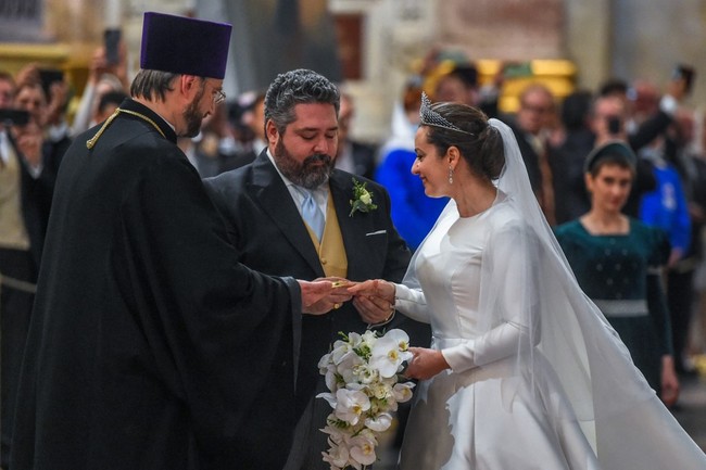 Mempelai wanita mengenakan gaun satin putih rancangan desainer Reem Acra, yang telah bekerja sama dengan Beyonce, Angelina Jolie, Madonna, dan Melania Trump. Cincin pertunangannya menggunakan batu permata ruby cabochon yang melambangkan cinta dan kemuliaan. Ada pula dua berlian yang melambangkan kemurnian dan kekuatan. Foto: dok. AFP/OLGA MALTSEVA