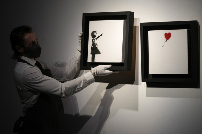 Members of staff hold up an artwork by British graffiti artist Banksy entitled 'Girl and Ballon' (two parts), during a pre-auction press viewing at Christie's auction house in London, Friday, Oct. 1, 2021. The diptych is expected to sell for 2,500,000 million pounds sterling (US, $3.5-4.8 million, euros 3-4.1 million). (AP Photo/Alastair Grant)
