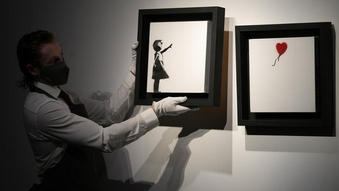 Wow! Karya Members of staff hold up an artwork by British graffiti artist Banksy entitled 'Girl and Ballon' (two parts), during a pre-auction press viewing at Christie's auction house in London, Friday, Oct. 1, 2021. The diptych is expected to sell for 2,500,000 million pounds sterling (US, $3.5-4.8 million, euros 3-4.1 million). (AP Photo/Alastair Grant)