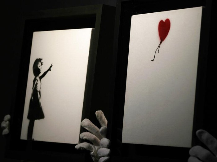 Members of staff hold up an artwork by British graffiti artist Banksy entitled Girl and Ballon (two parts), during a pre-auction press viewing at Christies auction house in London, Friday, Oct. 1, 2021. The diptych is expected to sell for 2,500,000 million pounds sterling (US, $3.5-4.8 million, euros 3-4.1 million). (AP Photo/Alastair Grant)