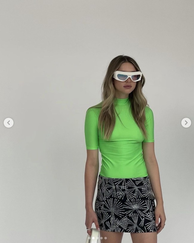 Eve Jobs mengenakan kaus hijau neon bergaya sporty, berpadu dengan rok mini hitam berdetail embellishment dalam debutnya sebagai model catwalk. Gaya Eve Jobs juga dilengkapi kacamata bergaya futuristik dan sepatu sendal bersol tebal. Foto: Dok. Instagram @ evecjobs