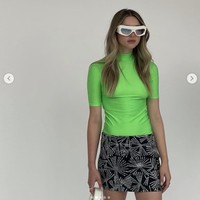 Eve Jobs mengenakan kaus hijau neon bergaya sporty, berpadu dengan rok mini hitam berdetail embellishment dalam debutnya sebagai model catwalk. Gaya Eve Jobs juga dilengkapi kacamata bergaya futuristik dan sepatu sendal bersol tebal. Foto: Dok. Instagram @ evecjobs