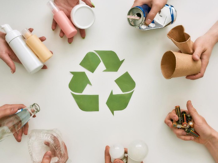 Top view of many hands holding different waste, garbage types with recycling sign made of paper in the center over white background. Sorting, recycling waste concept. Horizontal shot. Top view