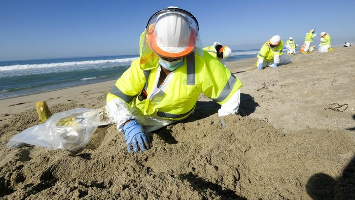 A worker in protective suits cleans the contaminated beach after an oil spill in Huntington Beach, Calif., on Tuesday, Oct. 5, 2021. The Coast Guard received the first report of a possible oil spill off the Southern California coast more than 12 hours before a company reported a major leak in its pipeline and a cleanup effort was launched, records show. (AP Photo/Ringo H.W. Chiu)