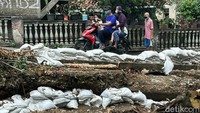 Kayu-kayu dibikin sedemikian rupa menyerupai pagar supaya bisa menahan karung-karung di pinggir kali berair cokelat itu.