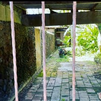 Pria bernama asli Junior John Rorimpandey itu hanya bisa mengabadikan rumah tersebut dari luar di depan pagar. Terlihat di balik pagar dengan tralis bergaya klasik ini, sebuah garasi berlantai batuan alam yang ditumbuhi rumput. (Foto: Instagram/@junarorimpandeyofficial)