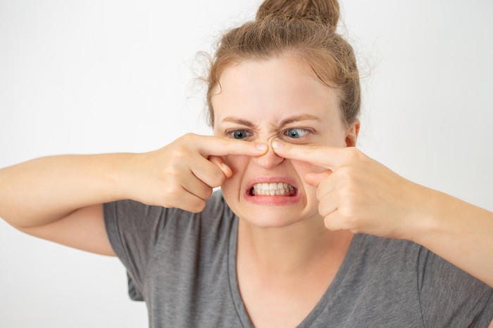 Young caucasian woman squeezing a pimple on her nose, funny facial expression on white background