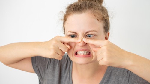 Young caucasian woman squeezing a pimple on her nose, funny facial expression on white background