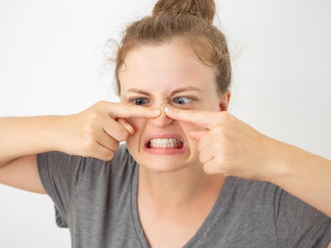 Young caucasian woman squeezing a pimple on her nose, funny facial expression on white background