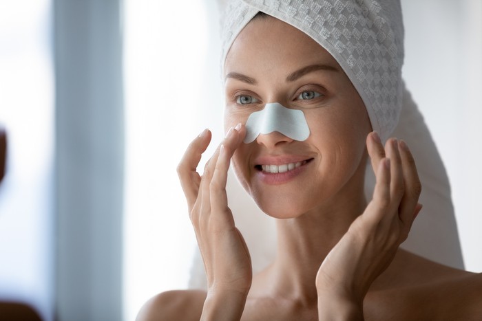 Close up 30s woman after shower with towel on head use white cleansing nose strips deep purifying treatment to unclog pores prevent remove blackheads, leaving skin clear and smooth, skincare concept