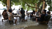 Sejumlah pengunjung tengah menyantap makanan di tengah banjir yang merendam sebuah restoran di kawasan Nonthaburi, dekat Bangkok, Thailand.
