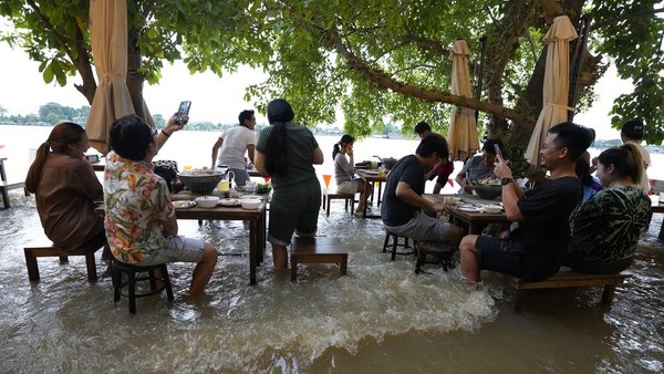 Sejumlah pengunjung tengah menyantap makanan di tengah banjir yang merendam sebuah restoran di kawasan Nonthaburi, dekat Bangkok, Thailand.