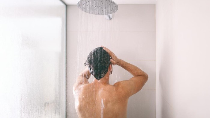 Man taking a shower washing hair with shampoo product under water falling from luxury rain shower head. Morning routine luxury hotel lifestyle guy showering. body care hygiene.