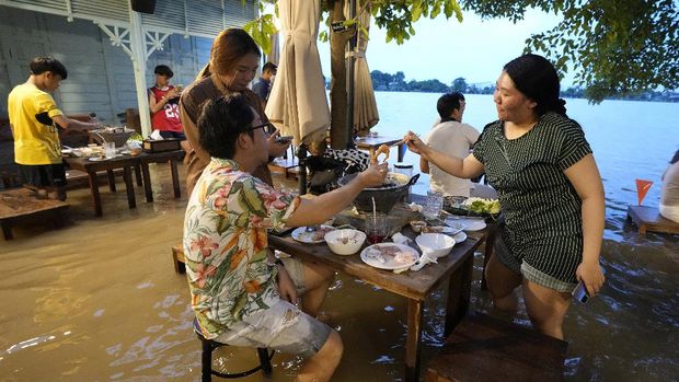 Customers of the riverside Chaopraya Antique Café enjoy themselves despite the extraordinary high water levels in the Chao Phraya River in Nonthaburi, near Bangkok, Thailand, Thursday, Oct. 7, 2021. The flood-hit restaurant has become an unlikely dining hotspot after fun-loving foodies began flocking to its water-logged deck to eat amid the lapping tide. Now, instead of empty chairs and vacant tables the “Chaopraya Antique Café” is as full as ever, offering an experience the canny owner has re-branded as “hot-pot surfing.” (AP Photo/Sakchai Lalit)