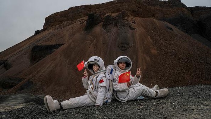 Sensasi Wisata di Gunung Berapi China Ala Astronot ULAN HADA, CHINA - OCTOBER 04: A couple wearing rented astronaut costumes hold hands as they walk together while visiting Volcano #6 of the the Ulan Hada volcano cluster during the Golden Week holiday on October 4, 2021 near Ulan Qab, Inner Mongolia Autonomous Region, China. The volcano cluster, which has seven volcanos, saw its last eruptions more than 10,000 years ago and is a popular tourist destination. (Photo by Kevin Frayer/Getty Images)