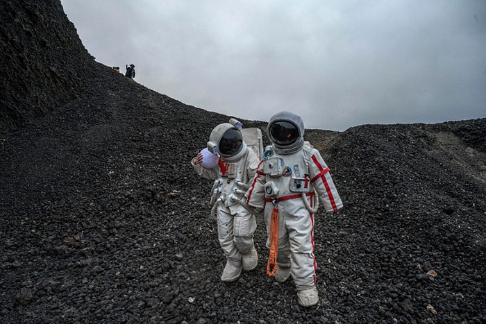 ULAN HADA, CHINA - OCTOBER 04: A couple wearing rented astronaut costumes hold hands as they walk together while visiting Volcano #6 of the the Ulan Hada volcano cluster during the Golden Week holiday on October 4, 2021 near Ulan Qab, Inner Mongolia Autonomous Region, China. The volcano cluster, which has seven volcanos, saw its last eruptions more than 10,000 years ago and is a popular tourist destination. (Photo by Kevin Frayer/Getty Images)