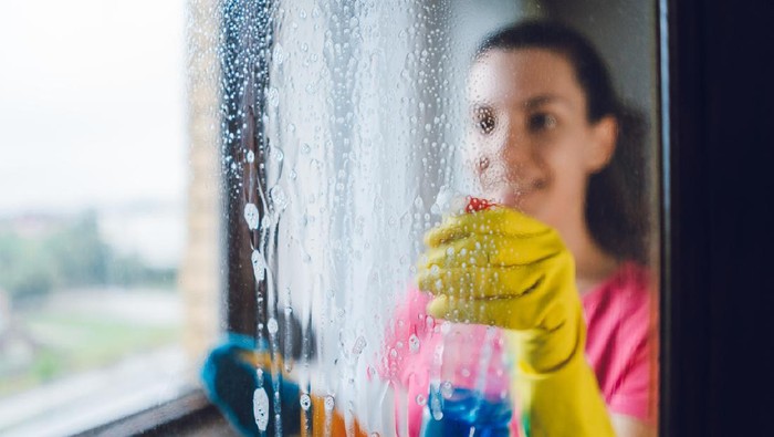 Young woman wiping windows at home