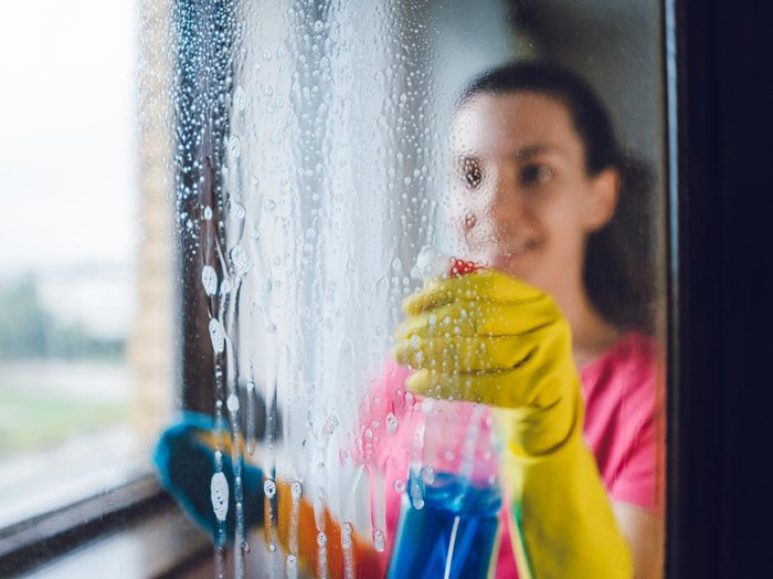 Young woman wiping windows at home