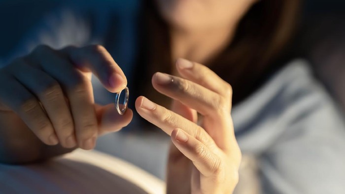 1290116690 Divorce concept - close up of asian sad depressed woman taking off her wedding ring on the bed
