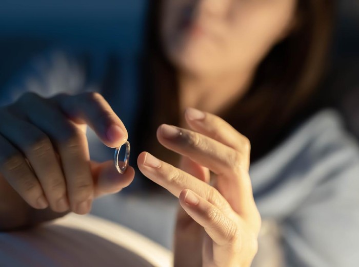 Divorce concept - close up of asian sad depressed woman taking off her wedding ring on the bed