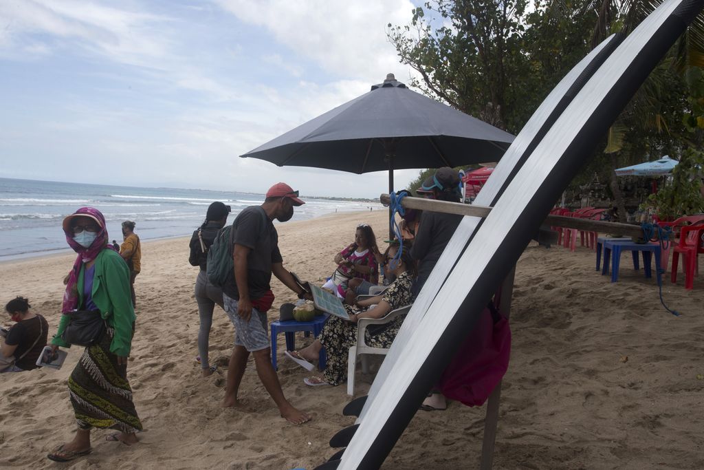 Beach vendors wait for customers at Kuta beach in Bali, Indonesia, Thursday, Oct. 14, 2021. The Indonesian resort island of Bali welcomed international travelers to its shops and white-sand beaches for the first time in more than a year Thursday - if they're vaccinated, test negative, hail from certain countries, quarantine and heed restrictions in public. (AP Photo/Firdia Lisnawati)