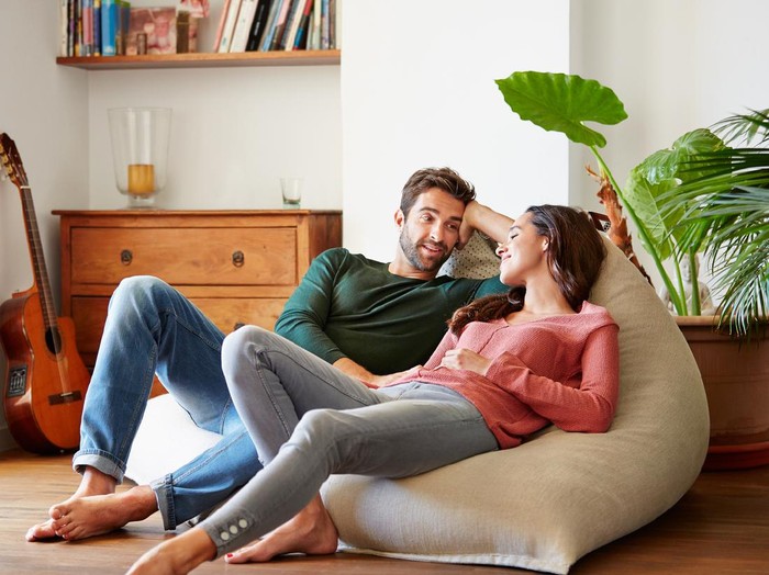 Ilustrasi pasangan Shot of a smiling young couple talking together while relaxing on a beanbag sofa at home