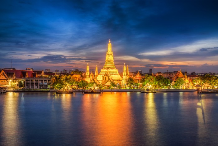 Long exposure photo of Wat Arun temple in front of Chao Phraya river in Bangkok at dusk. Thailand
