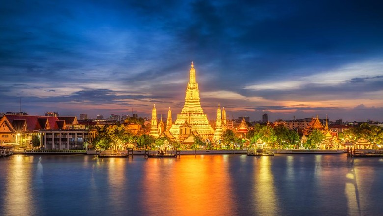 Long exposure photo of Wat Arun temple in front of Chao Phraya river in Bangkok at dusk. Thailand