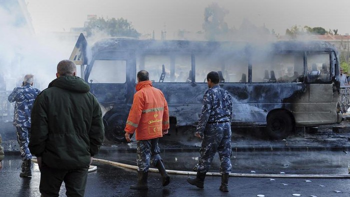 In this photo released by the Syrian official news agency SANA, Syrian firefighters and security officer check a burned bus at the site of a deadly explosion, in Damascus, Syria, Wednesday, Oct. 20, 2021. Two roadside bombs exploded near a bus carrying troops during the morning rush hour in the Syrian capital early Wednesday, killing and wounding several people, state TV reported. (SANA via AP)
