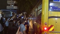 Deretan bus meninggalkan pintu belakang penjara, dengan para penumpang bersandar dari jendela dan melambai pada kerumunan orang yang berkumpul di luar.