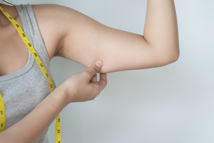 Young Asian woman feeling worried about her over weight problem and measuring her upper arm size by measuring tape.