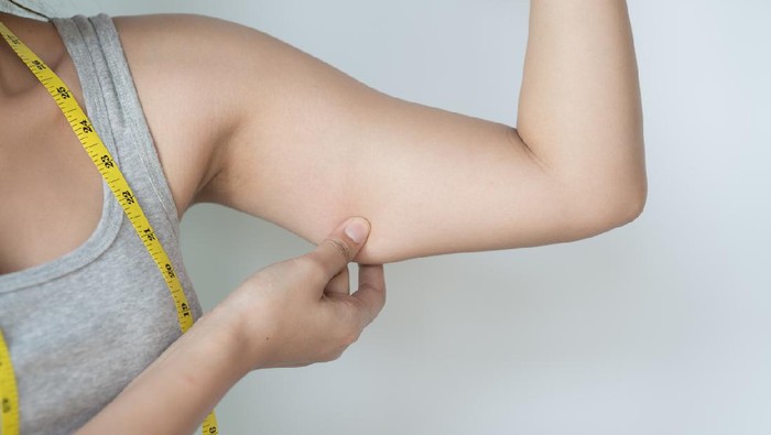 Young Asian woman feeling worried about her over weight problem and measuring her upper arm size by measuring tape.