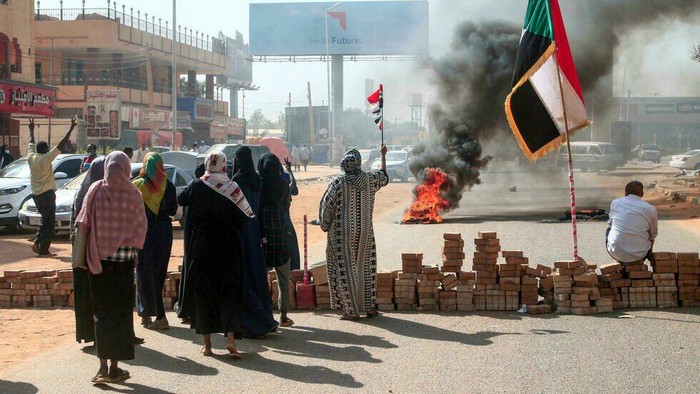 Sudanese protesters lift national flags next to a brick roadblock during a demonstration against the apparent military coup in the capital Khartoum, on October 25, 2021. © (AFP)