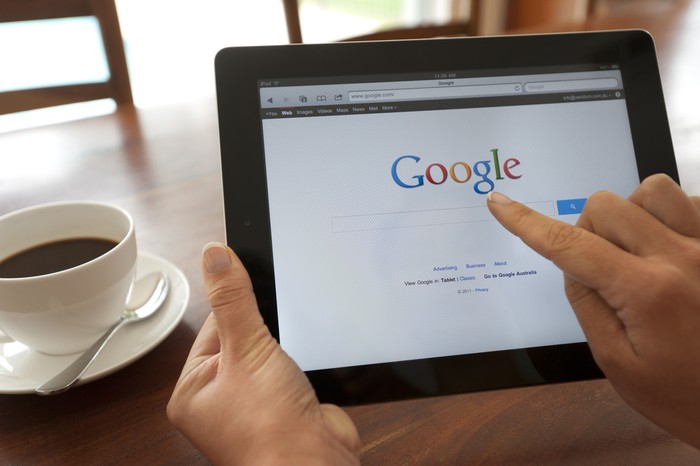 Sydney, Australia - October 28, 2011: Female hand holding an ipad showing Google. She is touching the screen. There is coffee on the dining table in the background.  This image shows the ipad being used in a casual environment.