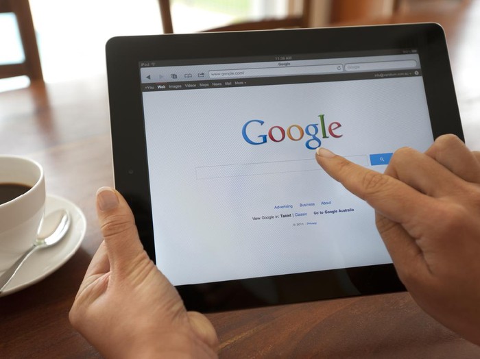 Sydney, Australia - October 28, 2011: Female hand holding an ipad showing Google. She is touching the screen. There is coffee on the dining table in the background.  This image shows the ipad being used in a casual environment.