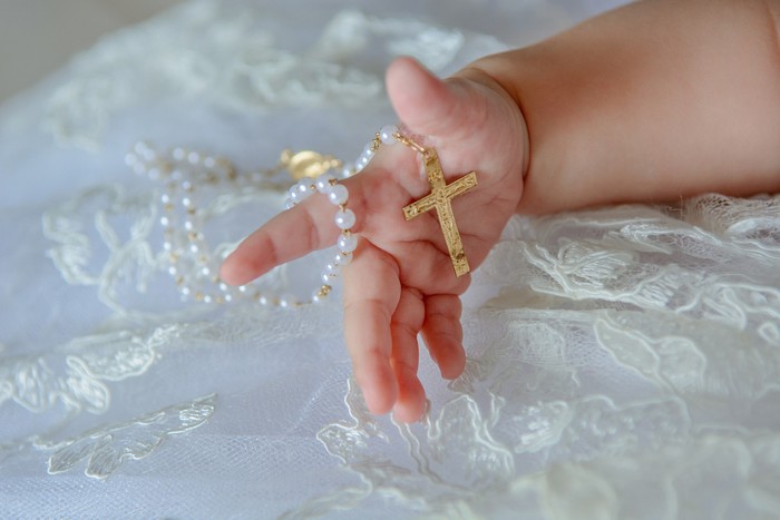 Childs hand with a crucifix on a white cloth.