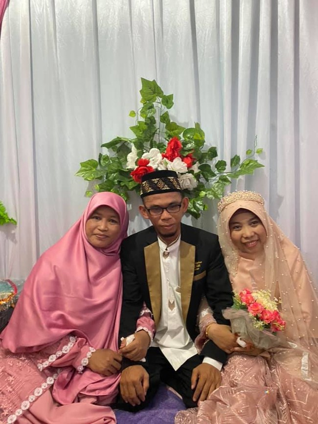 Dalam video tersebut terlihat, istri pertama memakai busana serba pink dan tampil tanpa makeup. Sedangkan istri kedua yang hari itu menjadi pengantin, mengenakan gaun dan veil wedding warna coral. Dan sang suami menggunakan jas serta peci hitam. Foto: Dok. Facebook Nana Ratnawati Palaha.