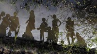 Anak-anak yang berdiri di atas tanggul lumpur kecil tercermin dalam genangan air, di Langic, Negara Bagian Bahr el Ghazal Utara, Sudan Selatan.  