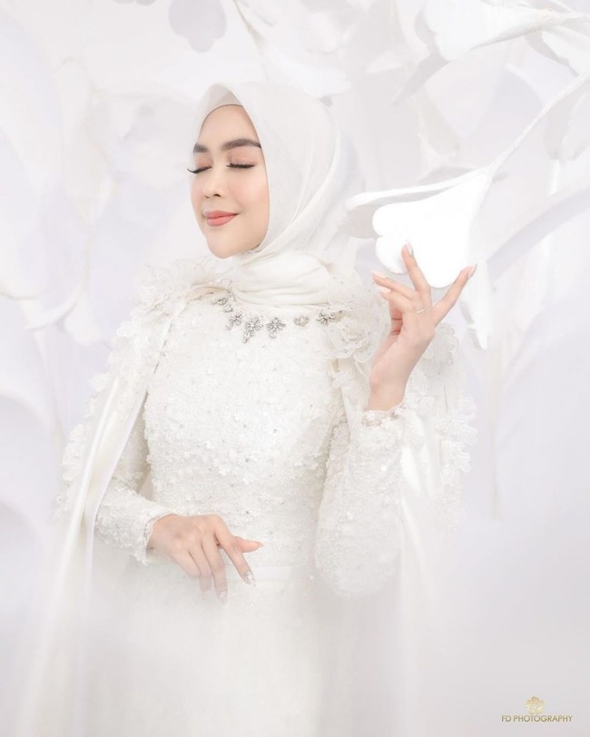 Ria Ricis tampil cantik dan memukau dengan pakaian serba putih. Pada bagian leher dress yang dikenakan oleh Ricis tampak dihiasi dengan kristal tempel yang membuat penampilannya semakin elegan. Untuk hijab, Ria memilih model segiempat yang simpel. Foto: Instagram/@fdphotography