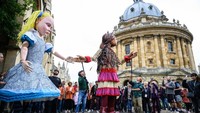 Alice dari kisah Alice in Wonderland juga digambarkan raksasa dan berjalan beriringan dengan Little Amal. Foto: Getty Images/Leon Neal