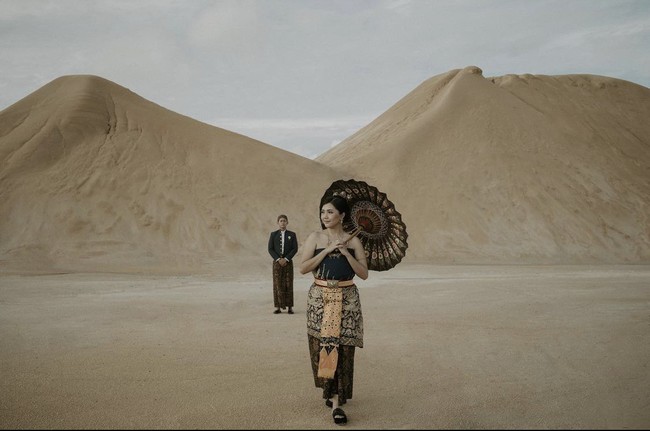 Foto prewedding di Gurun Pasir Desa Busung, Kepulauan Riau ini juga bisa menjadi inspirasi kamu. Sepasang calon pengantin mengenakan busana adat dilengkapi dengan payung tradisional yang cantik. Sosok pria seolah berjarak sambil memandang wanitanya yang ada di depan. Foto: Dok. Instagram @ceritatentangsenja.
