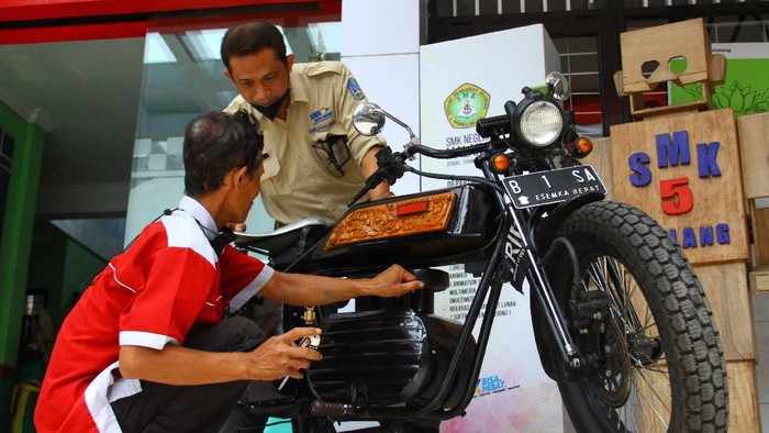 Kepala Sekolah Cone Kustarto (kanan) menunjukkan cara kerja purwarupa sepeda motor listrik hasil inovasinya di SMKN 5 Malang, Jawa Timur, Jumat (29/10/2021). Sepeda motor listrik tesebut dirakit dengan memanfaatkan baterai komputer jinjing bekas dan mampu melaju dengan kecepatan 70 kilometer per jam dengan lama pengisian ulang hanya selama 2 jam saja. ANTARA FOTO/Ari Bowo Sucipto/hp.