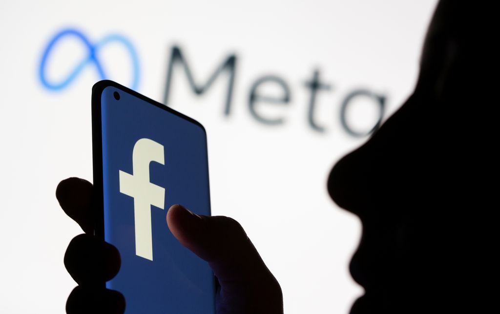 Woman holds smartphone with Facebook logo in front of a displayed Facebook's new rebrand logo Meta in this illustration picture taken October 28, 2021. REUTERS/Dado Ruvic/Illustration