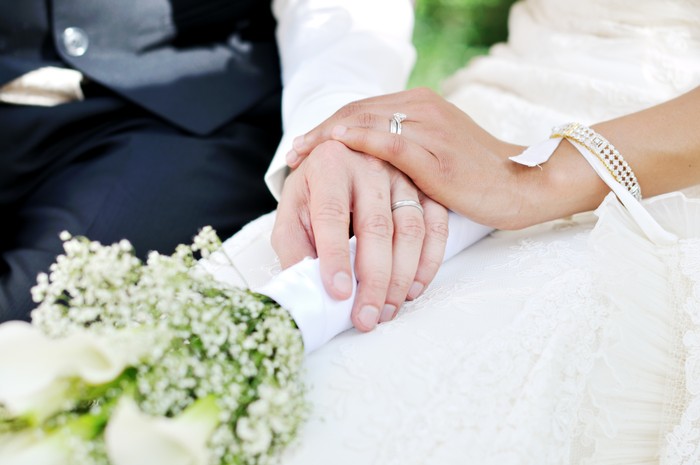Husband and wife hands on wedding, holding flowers.