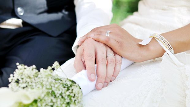 Husband and wife hands on wedding, holding flowers.