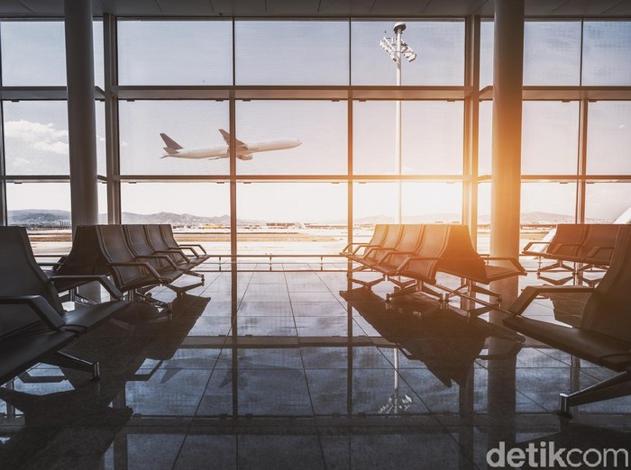 Wide-angle view of a modern aircraft gaining the altitude outside the glass window facade of a contemporary waiting hall with multiple rows of seats and reflections indoors of an airport terminal El Prat in Barcelona