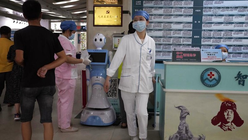 Chen Xiaofang, a nurse at the department of cardiovascular medicine the Guangdong Second Provincial General Hospital, stands next to a robot that delivers medicine in Guangzhou, in southern China's Guangdong province, Sunday, Sept. 26, 2021. The hospital in southern China's Guangdong Province is using 5G and IoT technologies to collect, transmit and monitor more data in real time, allowing healthcare workers to provide better medical service for patients. (AP Photo/Ng Han Guan)