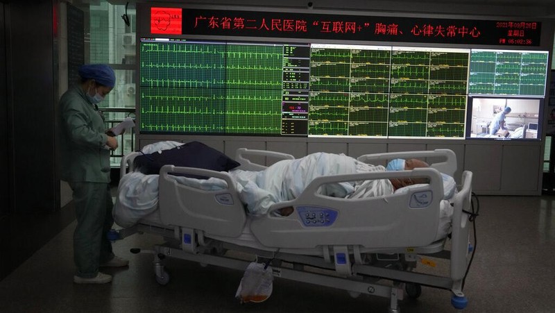 Chen Xiaofang, a nurse at the department of cardiovascular medicine the Guangdong Second Provincial General Hospital, stands next to a robot that delivers medicine in Guangzhou, in southern China's Guangdong province, Sunday, Sept. 26, 2021. The hospital in southern China's Guangdong Province is using 5G and IoT technologies to collect, transmit and monitor more data in real time, allowing healthcare workers to provide better medical service for patients. (AP Photo/Ng Han Guan)